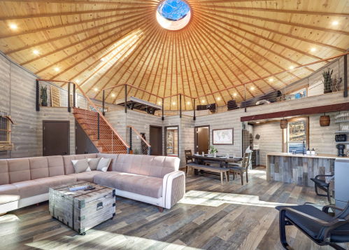 A spacious, modern interior of a round house with wooden walls, a skylight, and a cozy seating area.