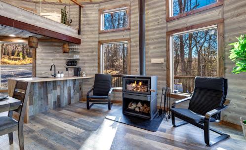 Cozy interior with large windows, a modern fireplace, and two chairs, surrounded by wooden walls and flooring.