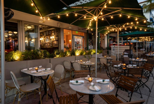 Outdoor dining area with tables, chairs, and string lights, creating a cozy atmosphere at a restaurant.