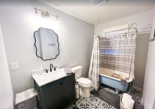 A modern bathroom featuring a marble vanity, a shower curtain, a bathtub, and patterned floor tiles.