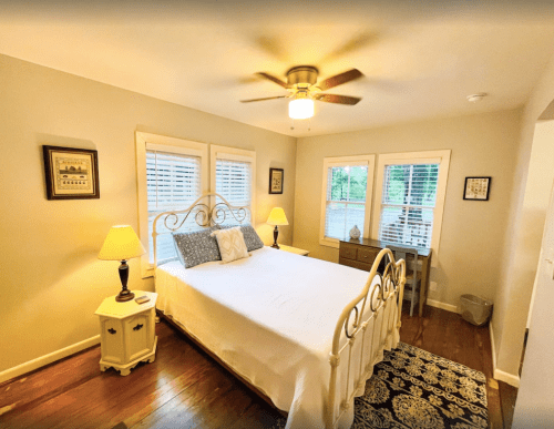 Cozy bedroom with a white bed, ceiling fan, two windows, and warm lighting from lamps on nightstands.