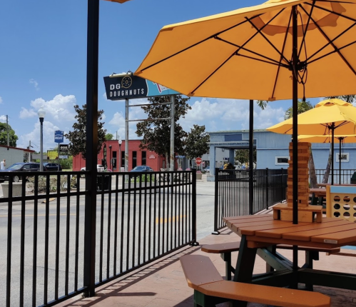 Outdoor seating area with yellow umbrellas, overlooking a street with shops and a sign for DG Doughnuts.