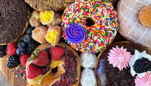 A colorful assortment of donuts topped with sprinkles, frosting, and fruit, surrounded by fresh berries on a wooden platter.