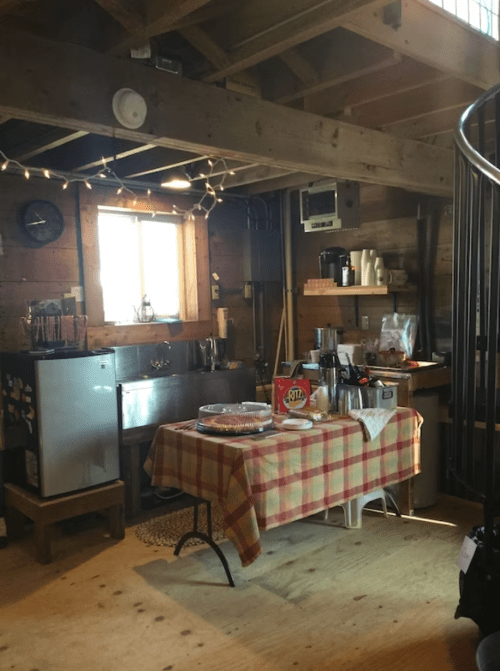 Cozy kitchen area with a table, snacks, and a spiral staircase, featuring wooden walls and warm lighting.