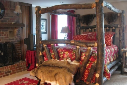 Cozy rustic bedroom featuring a log bed, red floral bedding, and animal hides on the floor. Warm, inviting atmosphere.