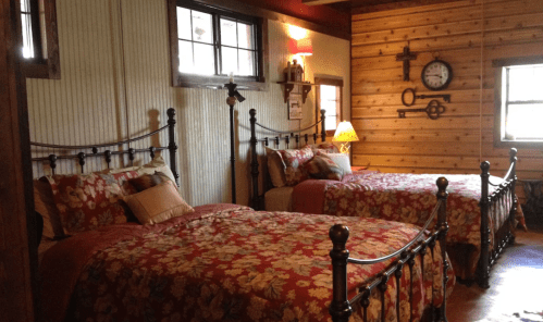 Cozy bedroom with two floral-patterned beds, wooden walls, and warm lighting.