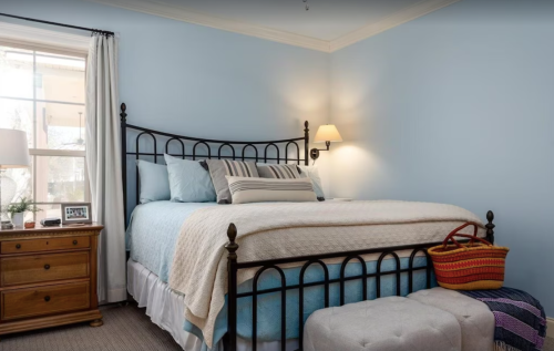 Cozy bedroom with a metal bed, light blue walls, a nightstand, and a woven basket at the foot of the bed.
