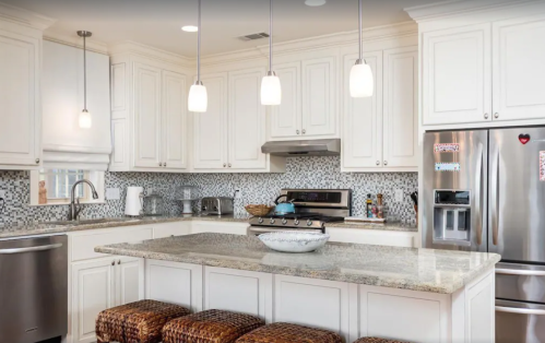 Modern kitchen with white cabinets, granite countertops, stainless steel appliances, and pendant lighting.