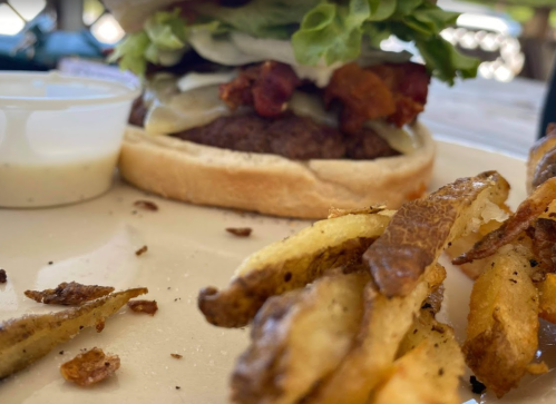 A close-up of a burger with lettuce, onions, and bacon, served with a side of crispy fries and a dipping sauce.