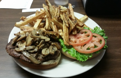 A plate with a burger topped with mushrooms, lettuce, and tomato, accompanied by a side of golden French fries.