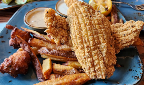 A plate of crispy fried fish fillets served with golden fries and dipping sauces.