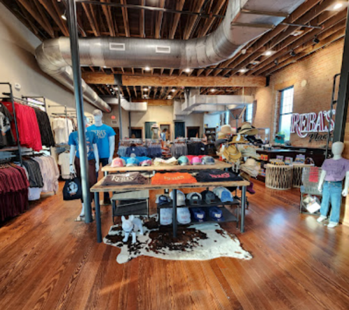 A retail store interior featuring clothing displays, hats, and mannequins in a spacious, well-lit environment.