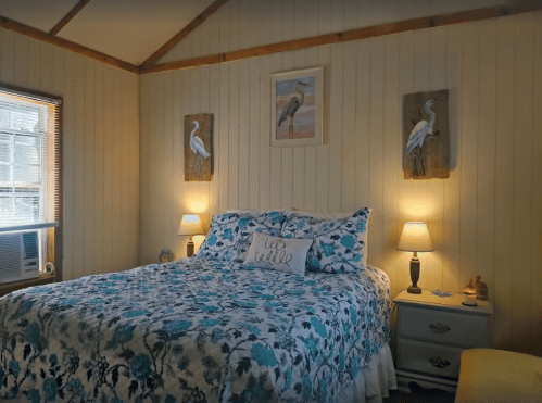 Cozy bedroom with a floral bedspread, two lamps, and bird-themed artwork on the walls.