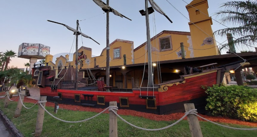 A colorful pirate ship-themed restaurant with sails, set against a clear sky and surrounded by greenery.