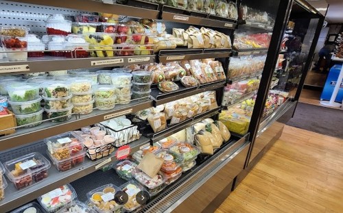 A display case filled with various packaged salads, fruits, and snacks in a grocery store.