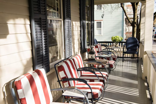 A cozy porch with striped chairs, a small table, and sunlight casting shadows on the floor.