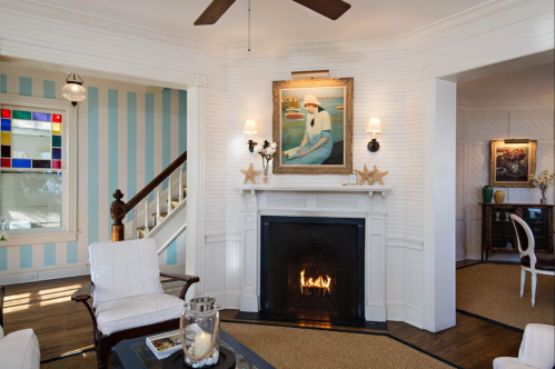 Cozy living room with a fireplace, artwork, and blue-striped walls, featuring comfortable seating and decorative accents.