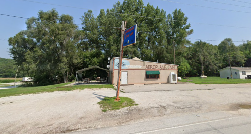 A small roadside building with a sign reading "Aeroplane Joint," surrounded by trees and gravel.
