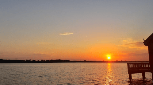 A serene sunset over a calm lake, with warm orange and yellow hues reflecting on the water.