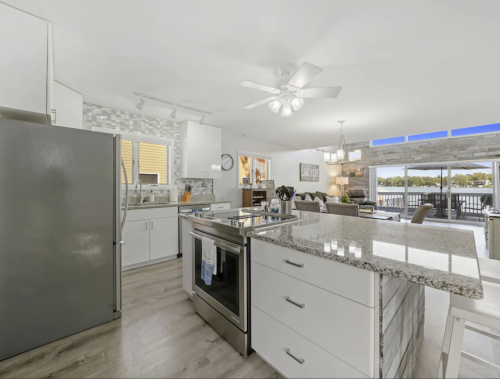 Modern kitchen with stainless steel appliances, granite countertops, and an open layout overlooking a living area and water view.
