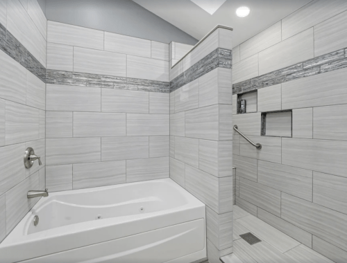 Modern bathroom featuring a walk-in shower with gray tiles and a white bathtub. Bright and spacious design.