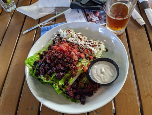 A colorful salad with lettuce, tomatoes, bacon bits, cheese, and a side of dressing, accompanied by a glass of beer.