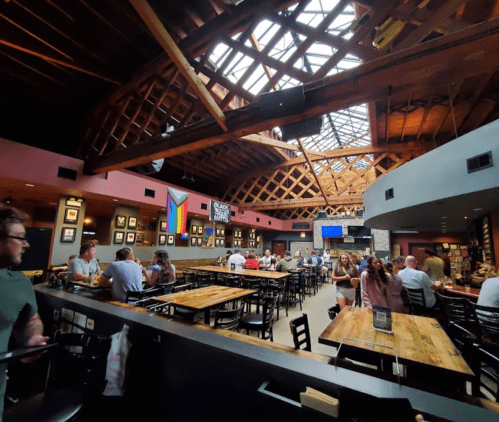 Interior of a lively restaurant with wooden beams, a skylight, and patrons dining at tables. Colorful decor on the walls.