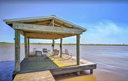 A wooden dock with a covered seating area overlooking a calm body of water under a clear blue sky.