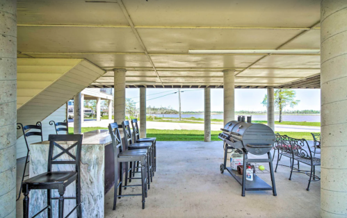 Outdoor patio area with bar stools, a grill, and a view of the lawn and water beyond.