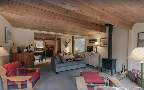 Cozy living room with wooden beams, a wood stove, and comfortable seating, featuring rustic decor and warm lighting.