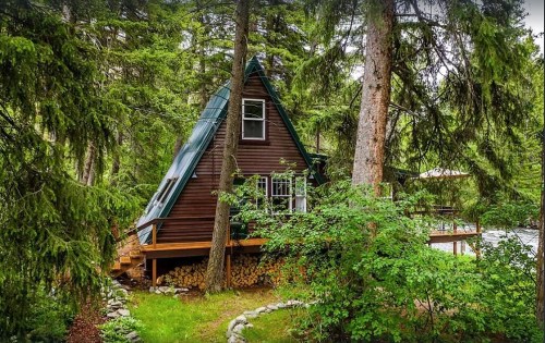 A cozy A-frame cabin nestled among tall trees, surrounded by greenery and a wooden deck.