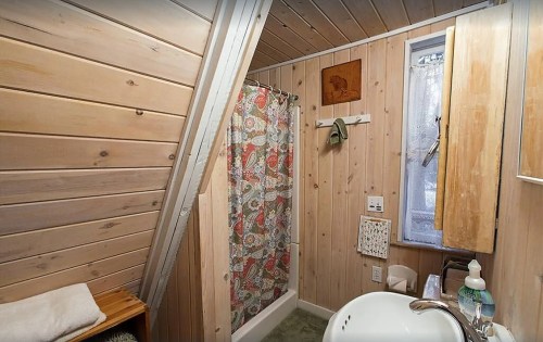 Cozy bathroom with wooden walls, a shower curtain, and a small window, featuring rustic decor and a towel rack.