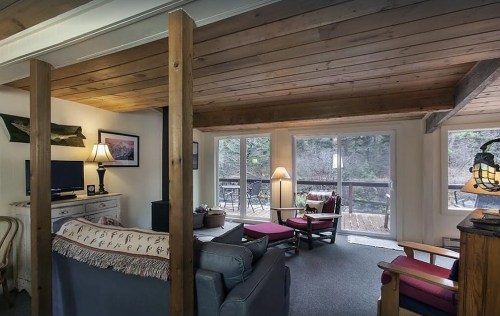 Cozy living room with wooden beams, a sofa, armchairs, and large windows overlooking a natural view.