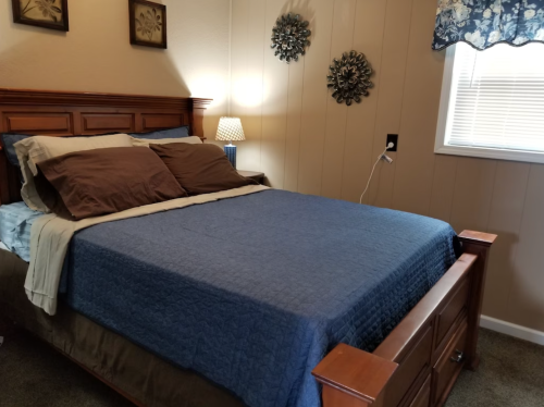 Cozy bedroom featuring a wooden bed with blue bedding, decorative wall art, and a bedside lamp.