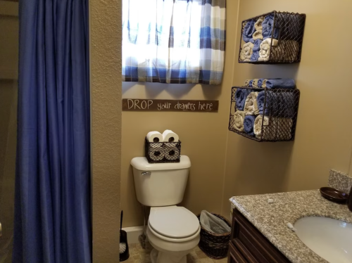 A cozy bathroom featuring a toilet, sink, and shelves with neatly folded towels, plus a humorous sign on the wall.
