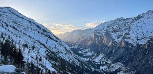 Snow-covered mountains and a valley under a clear sky, with the sun setting in the background.