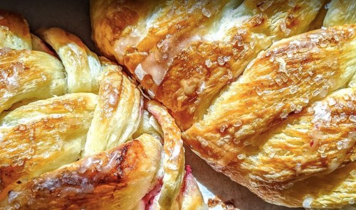 Close-up of golden, flaky pastries with a shiny glaze and sugar crystals, showcasing a braided design.