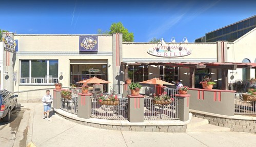 Exterior view of a Mediterranean grill with outdoor seating and potted plants, featuring a sunny atmosphere.