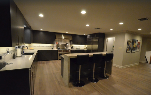 Modern kitchen with dark cabinetry, stainless steel appliances, and a central island with three black bar stools.