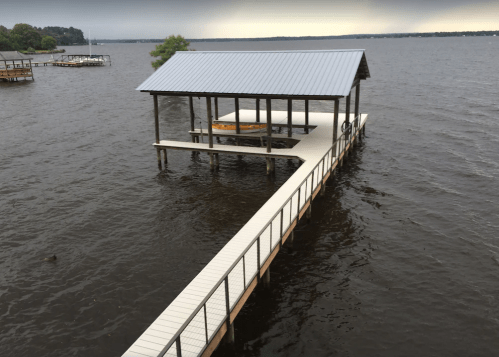 A wooden dock with a covered area extends over a calm lake, surrounded by dark water and a cloudy sky.