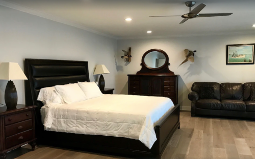 A modern bedroom featuring a large bed, nightstands, a dresser, a mirror, and a leather couch.