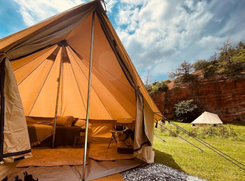 A spacious tent set up in a grassy area, with a cozy interior and a second tent visible in the background under a cloudy sky.