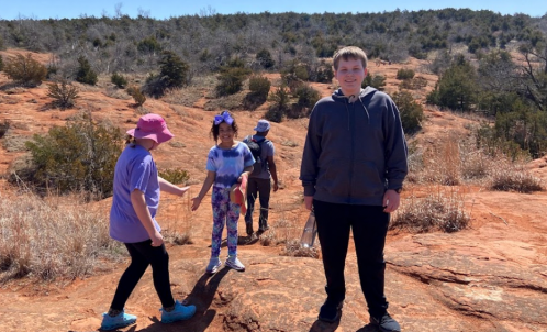 A group of children playing on rocky terrain, with trees and hills in the background on a sunny day.