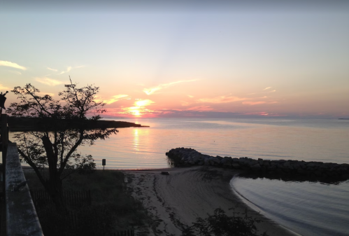 A serene beach at sunset, with calm waters, a rocky jetty, and soft clouds in the sky.