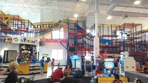 A colorful indoor play area with climbing structures, arcade games, and families enjoying their time together.