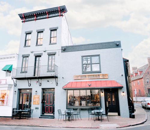 A charming three-story building with a sign reading "Iron Rooster," featuring outdoor seating and a modern facade.