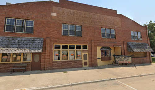 A brick building with multiple windows and a sign, featuring a rustic facade and a sidewalk in front.