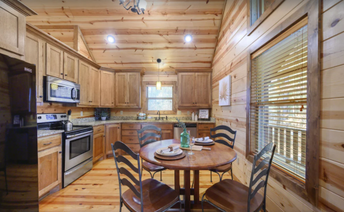 Cozy wooden kitchen with a round table set for two, featuring stainless steel appliances and warm, rustic decor.