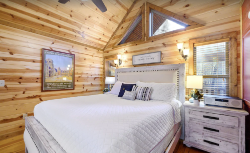 Cozy bedroom with wooden walls, a large bed, bedside lamps, and a window with a triangular design.