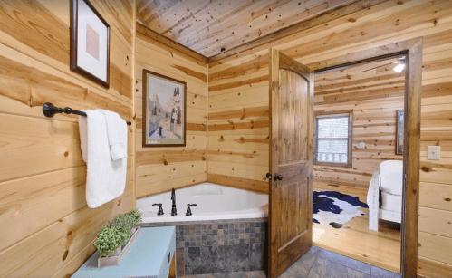 Cozy bathroom with wooden walls, a tub, and a door leading to a bedroom, featuring a cowhide rug.